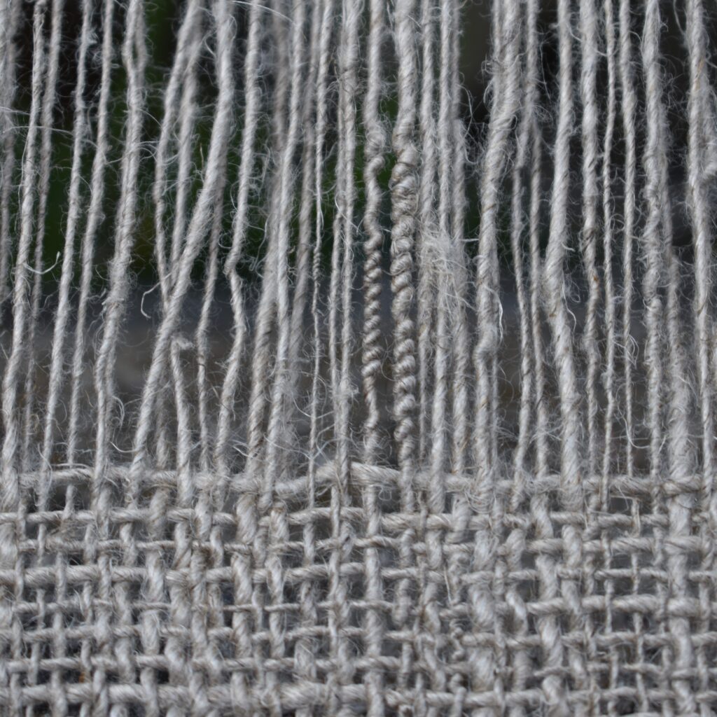 Handspun flax woven into brown linen fabric. Warp threads are visible above the woven fabric.